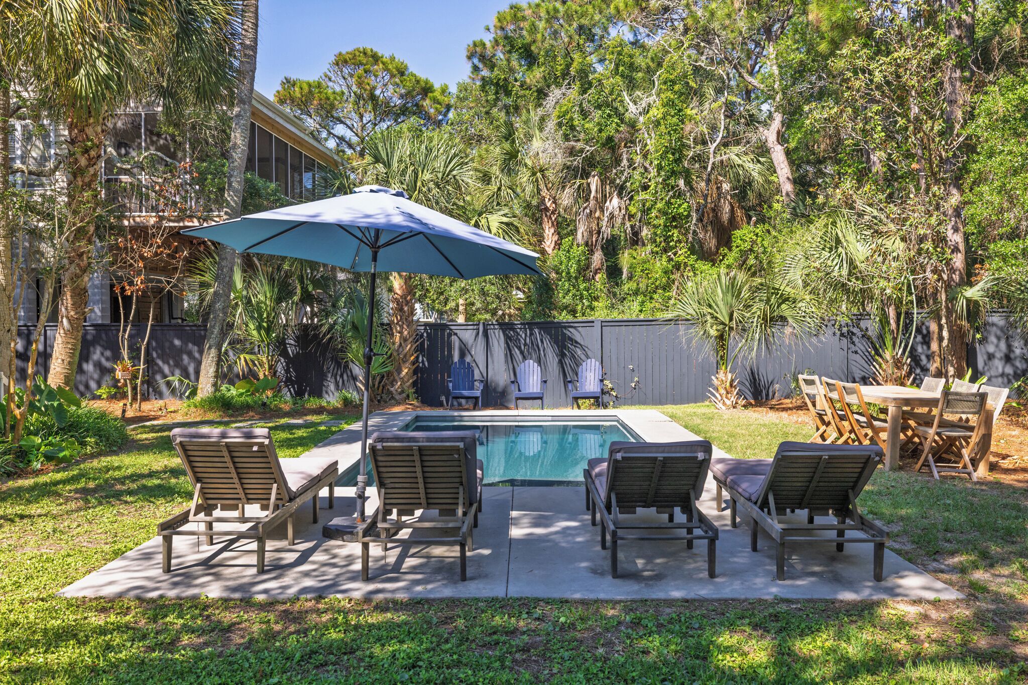 A backyard with a swimming pool, lounge chairs, and a dining table.