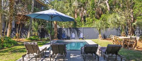 A backyard with a swimming pool, lounge chairs, and a dining table.