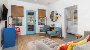 Een kamer met een blauwe deur, twee blauwe stoelen, een grijze bank, een klein tafeltje en een televisie op een meubel.'