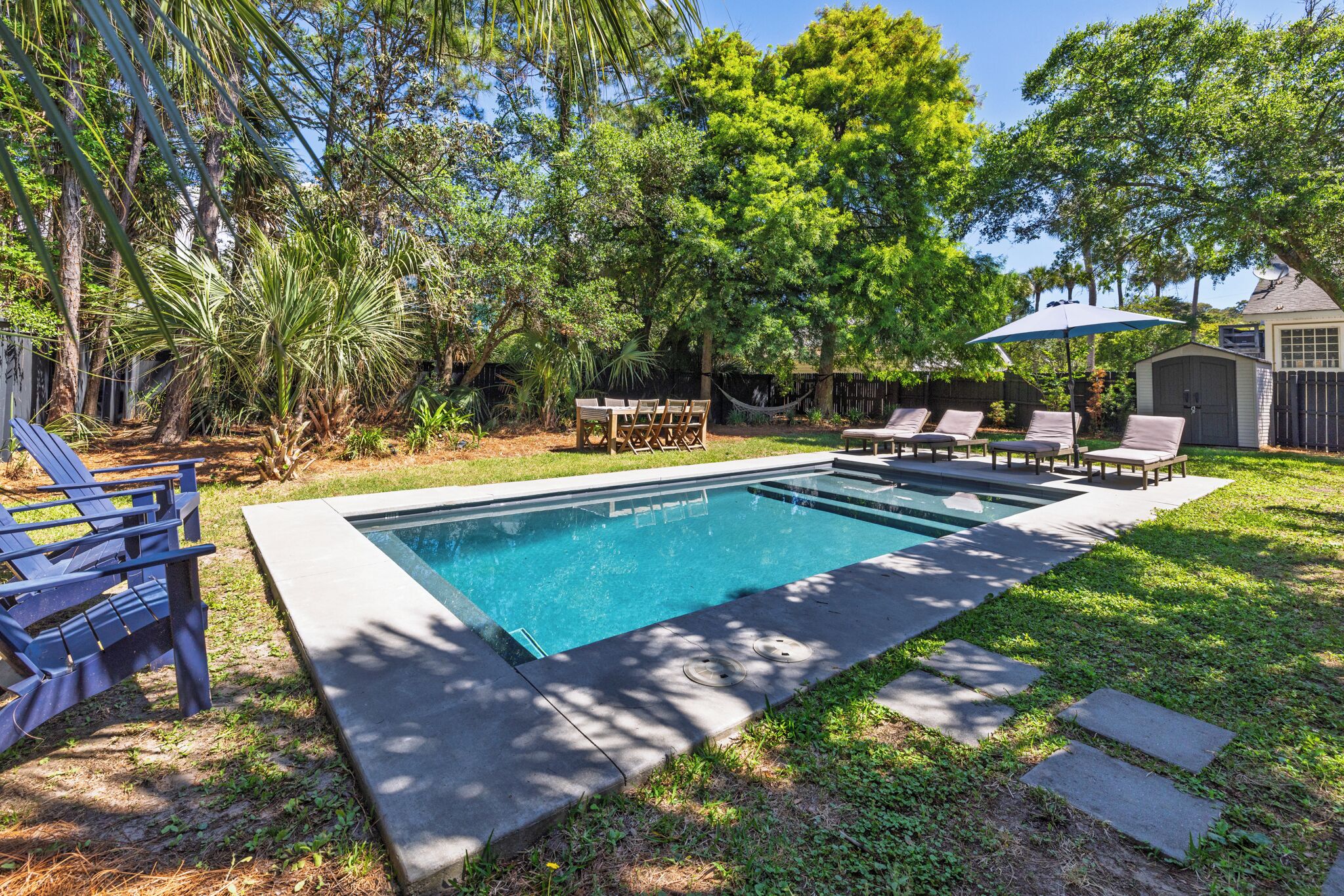 A rectangular swimming pool with a concrete edge, surrounded by a grassy area and trees.