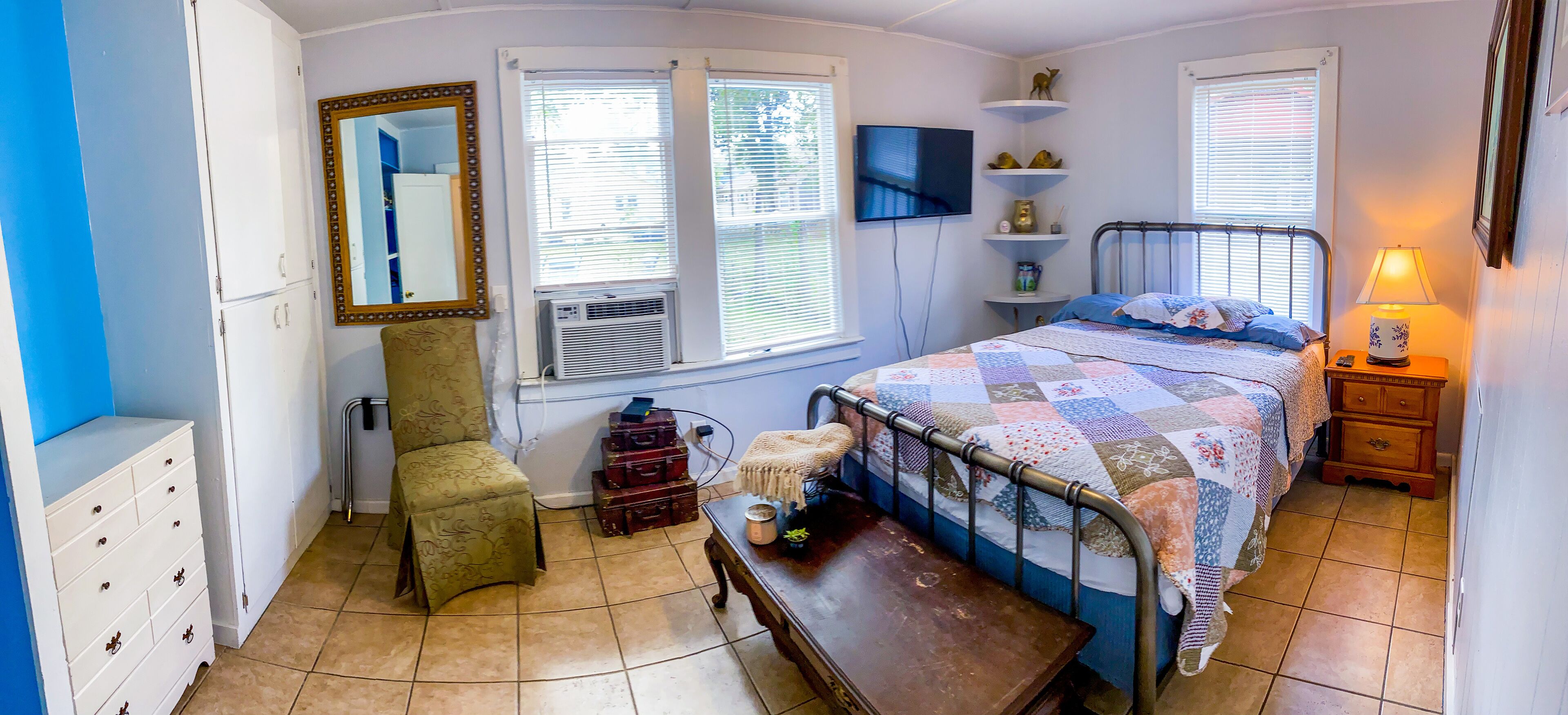 A bedroom with a bed, dresser, chair, and a TV on the wall.
