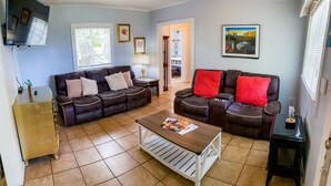 A living room with two sofas, a coffee table, and a TV. There is a window with blinds, a lamp, and a painting on the wall.