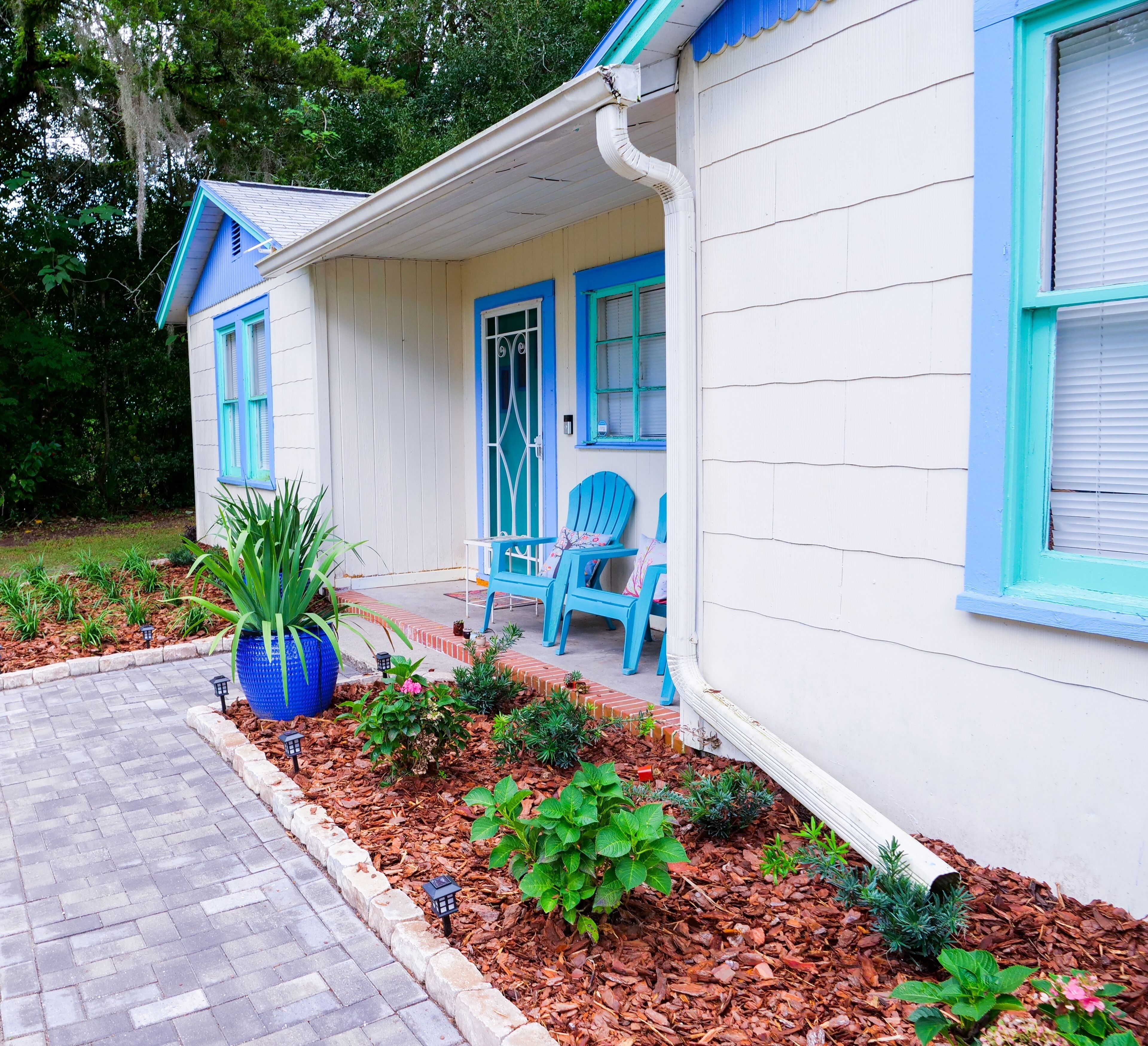 Une maison avec un porche, des chaises bleues et un grand pot de fleurs bleu.