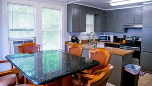 A kitchen with a dining area, featuring a granite countertop, wooden chairs, and grey cabinets.