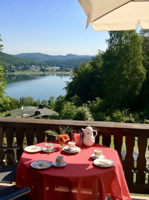 A table set with tea cups, plates, and a teapot on a red tablecloth, overlooking a lake with a view of a town and hills in the distance. - House with lake view and terraces - spacious (Edertal - Bringhausen)