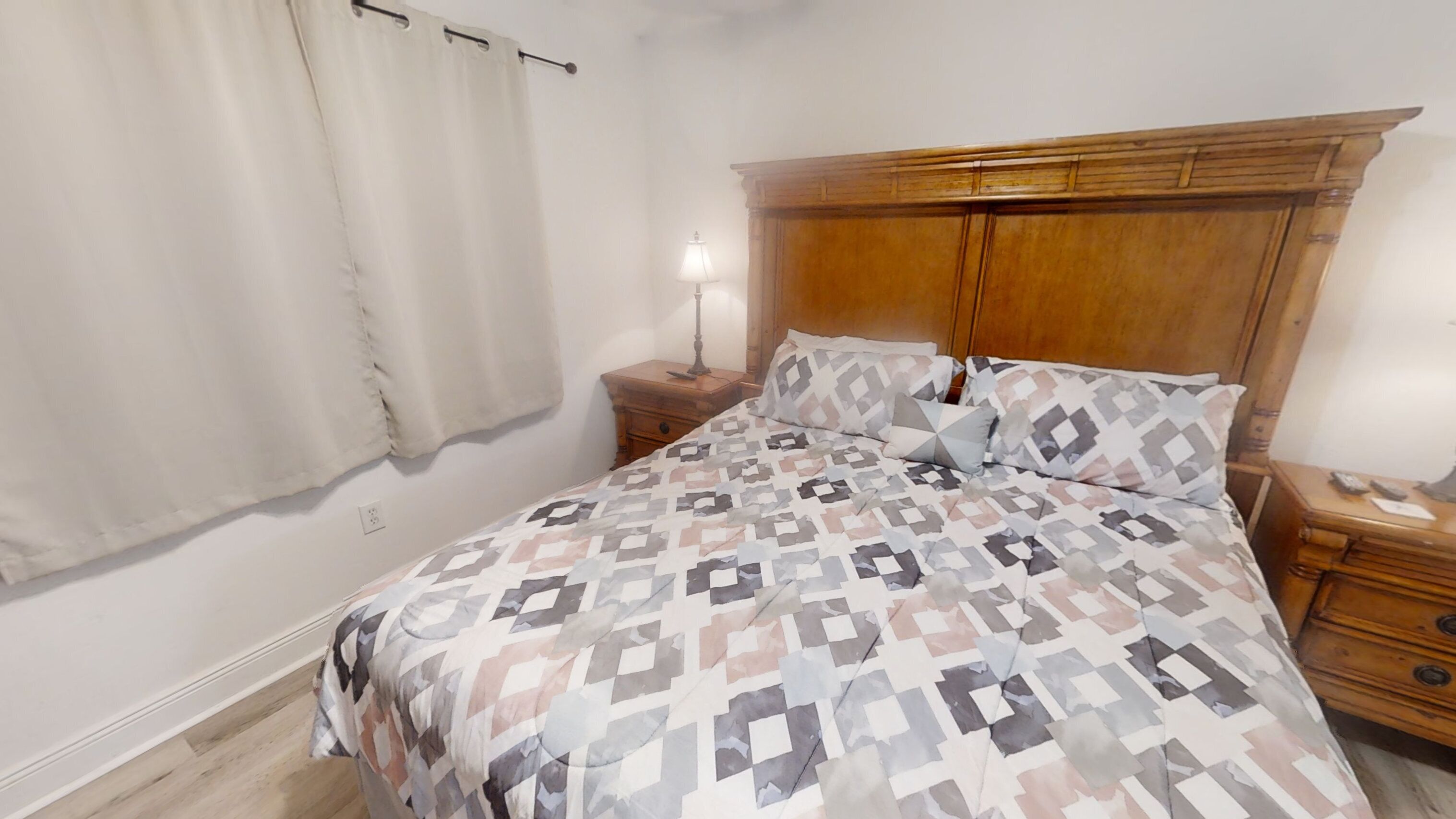 Una camera da letto con una coperta a motivi, una testiera in legno, comodini e una lampada.