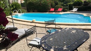 A swimming pool with lounge chairs and a table, surrounded by greenery and buildings. - Two bedrooms for six people, swimming pool in Hérault (Roujan)