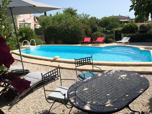 A swimming pool with lounge chairs and a table, surrounded by greenery and buildings.