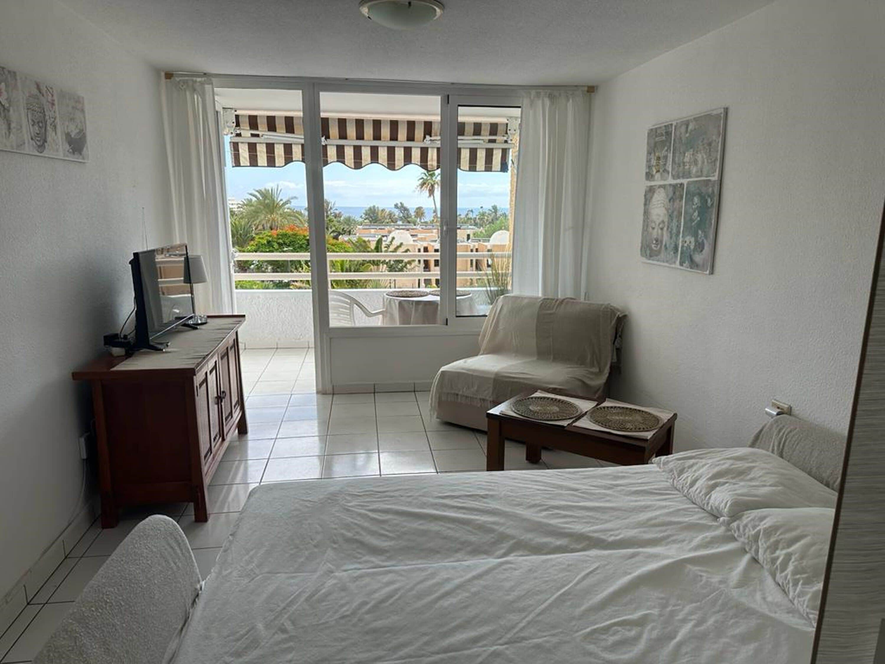 A hotel room with a bed, a desk with a computer, a chair, and a view of the outdoors.