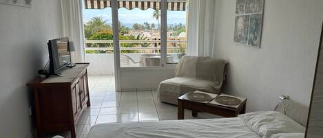A hotel room with a bed, a desk with a computer, a chair, and a view of the outdoors.