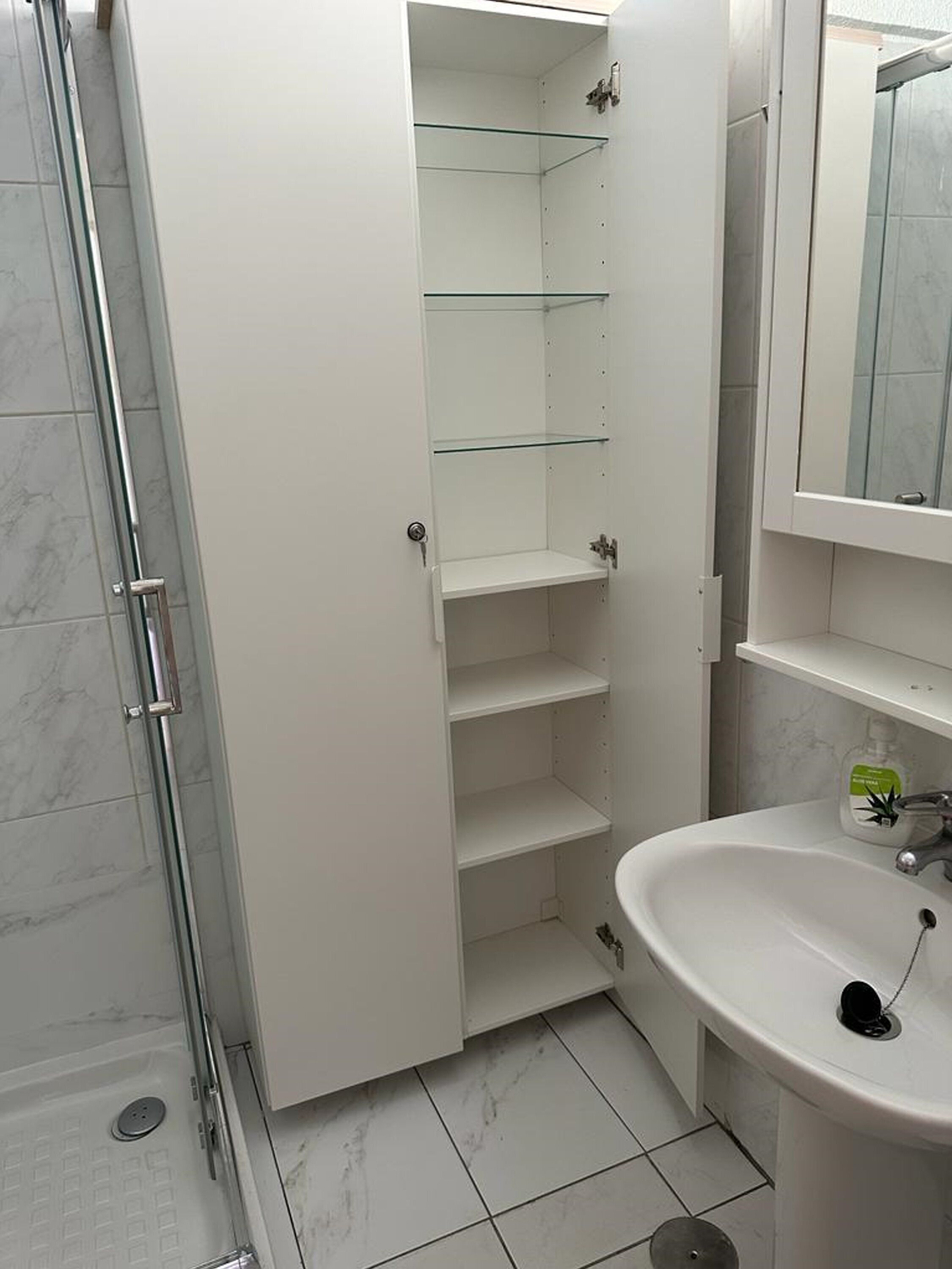 Un baño con cabina de ducha de vidrio, un lavabo blanco y un espejo sobre él.