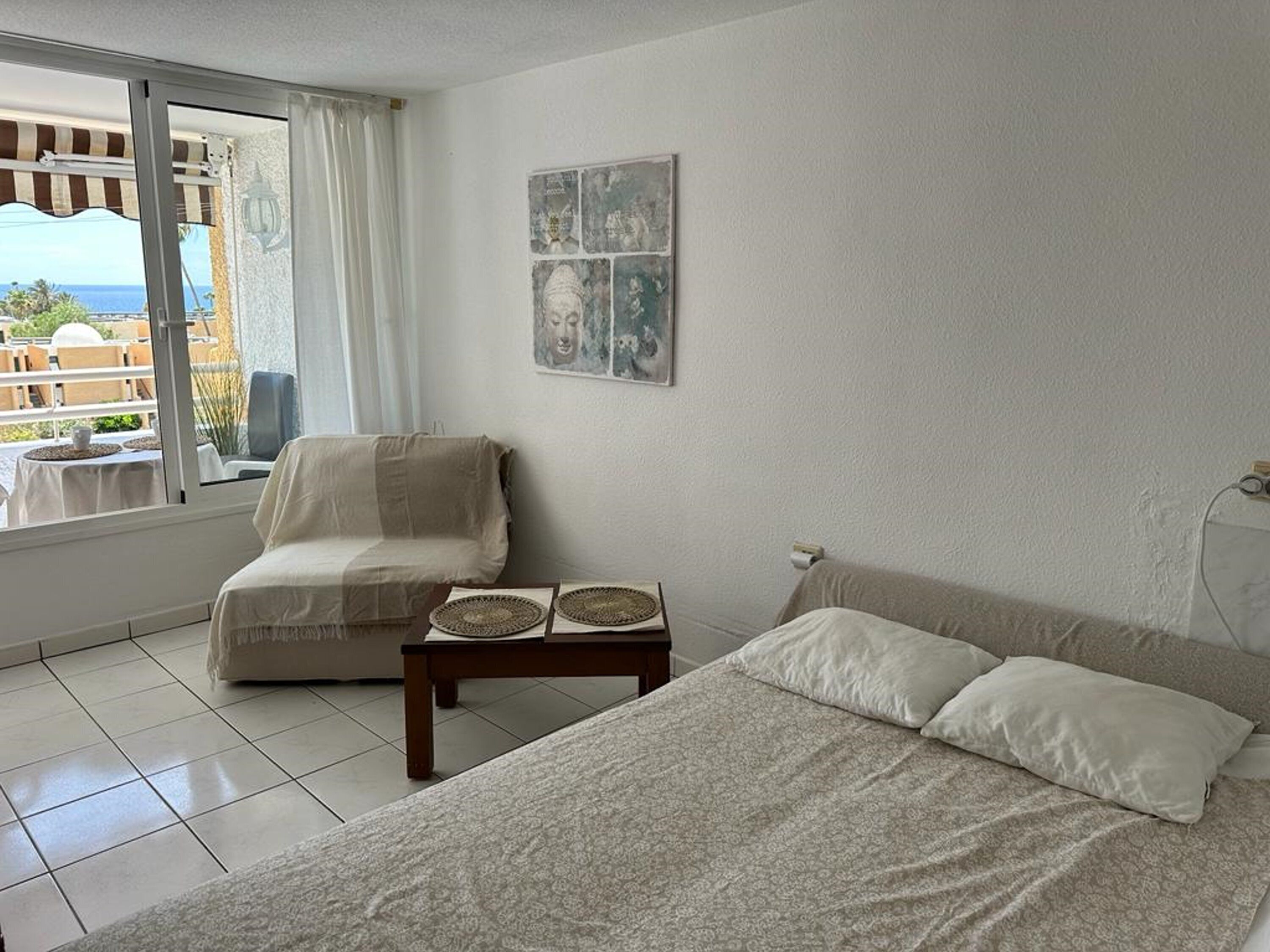 A bedroom with a bed, a chair, and a small table. There is a window with a view of the outside.