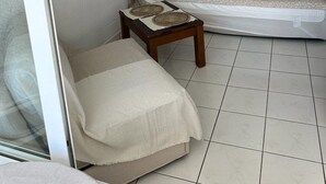 Et soveværelse med seng, natbord og stol. Der er et vindue med gardiner, en væg med kunst og en dør til et andet rum.