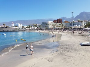 A beach with clear blue water, people swimming and walking, and buildings in the background. - Borinquen just 280 meters to the beach, balcony with sea view, heated pool, wifi (Costa Adeje)