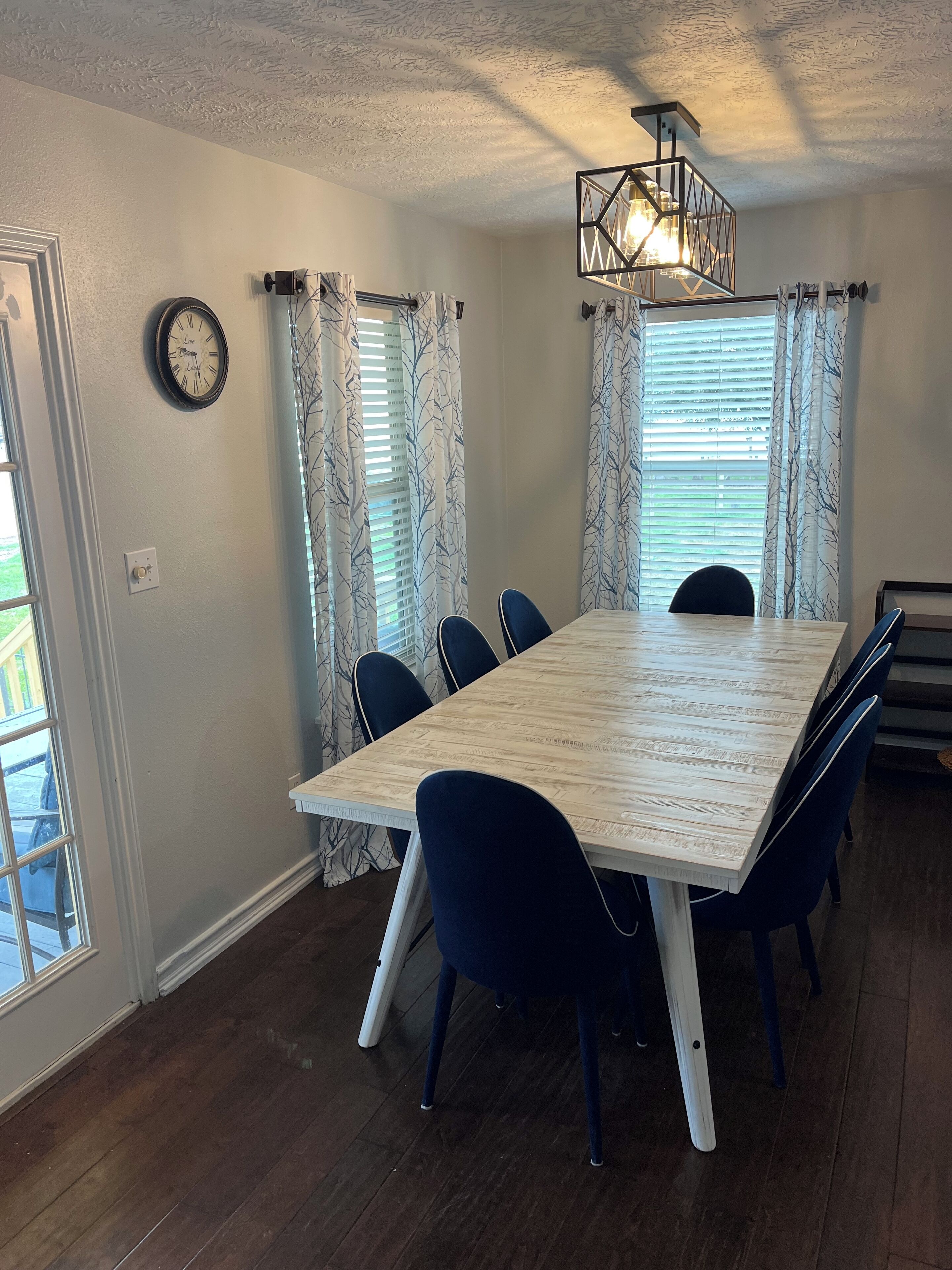 A dining area with a rectangular table, six chairs, a wall clock, and a ceiling light fixture.