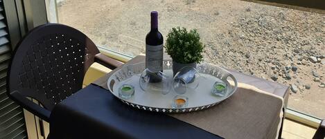 A balcony with a table set for two, featuring a bottle of wine, glasses, and a small potted plant.