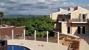 Una casa moderna de dos pisos con piscina, rodeada de vegetación y montañas al fondo.