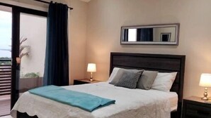Un dormitorio con cama, mesita de noche, espejo y vistas al exterior.