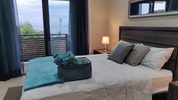 Un dormitorio con cama, mesita de noche con lámpara y vistas al exterior a través de una puerta corredera.