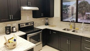 Una cocina moderna con armarios oscuros, una estufa de acero inoxidable, horno empotrado, una ventana con vista a la calle y un lavamanos con grifo.