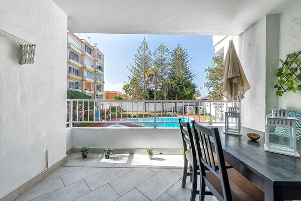 Un balcon donnant sur une piscine, un coin repas avec des chaises et une rambarde.
