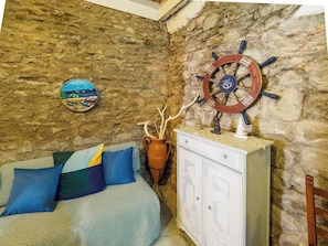 Une pièce avec un mur en pierre, un lit agrémenté d’oreillers bleus et multicolores, une armoire blanche et un élément décoratif en forme de roue de navire.
