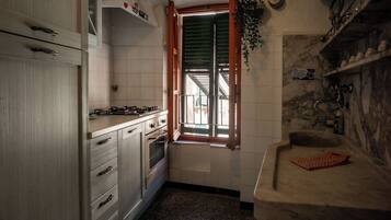 A kitchen with white cabinets, a gas stove, a window with wooden shutters, and a marble countertop.