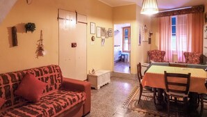 Un salon avec un canapé, une table à manger entourée de chaises, une cuisine à l’arrière-plan et un escalier menant à un autre niveau.