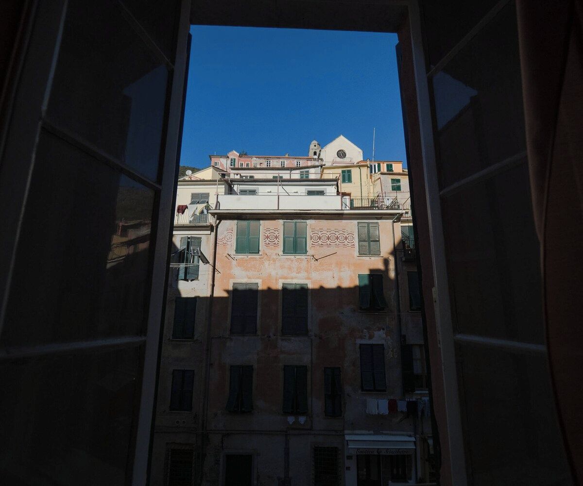 Une vue à travers la fenêtre d’un immeuble à étages, doté de balcons, avec un ciel bleu dégagé.