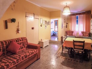 Een woonkamer met een bank, eettafel, stoelen en een keuken op de achtergrond.