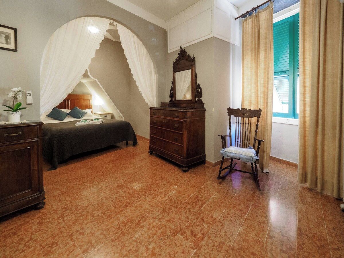 Un dormitorio con cama, cómoda, silla y ventana con cortinas.