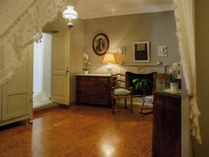 Une pièce avec un plancher en bois, un bureau avec une lampe, une chaise, une commode et une cheminée.