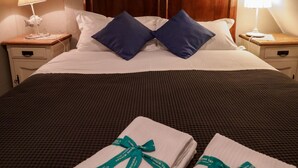 Un lit bien fait, avec du linge de lit blanc et deux oreillers bleus, une tête de lit en bois et deux tables de chevet avec des lampes.
