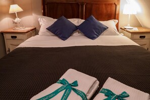Un lit bien fait, avec du linge de lit blanc et deux oreillers bleus, une tête de lit en bois et deux tables de chevet avec des lampes.