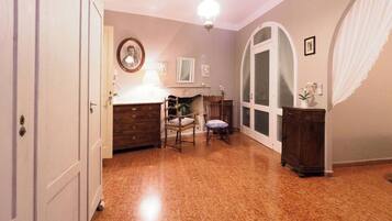 A room with a wooden floor, a desk with a lamp, a chair, a mirror, and a large arched window.