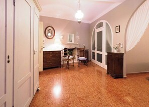 Een kamer met een houten vloer, een bureau met een lamp, een stoel, een spiegel en een groot, rondboogvormig raam.