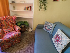 Een woonkamer met een gestreept fauteuil, een blauwe bank met decoratieve kussens, een boekenkast en een hangende plant.