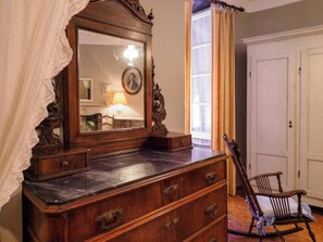 A wooden dresser with drawers and a mirror, a chair, and a door in a room with a window and curtains.