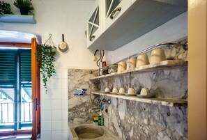 A kitchen with marble walls, a sink, and shelves with cups and plates.