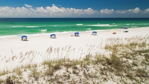 A beach with white sand, clear turquoise water, and a few umbrellas providing shade. - Coastal Soul Beach Seascape Resort Pools (Miramar Beach)