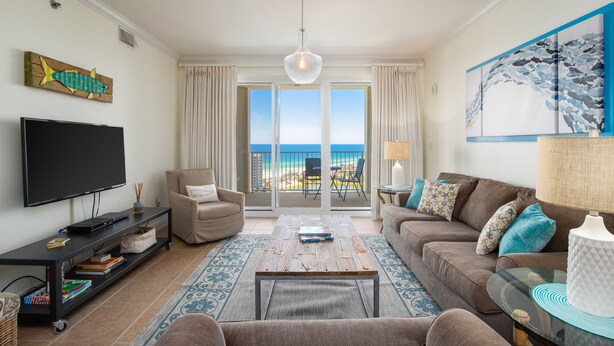 A living room with a flat-screen TV, a sofa, a coffee table, and a view of the ocean through large sliding doors. - Coastal Soul Beach Seascape Resort Pools (Miramar Beach)