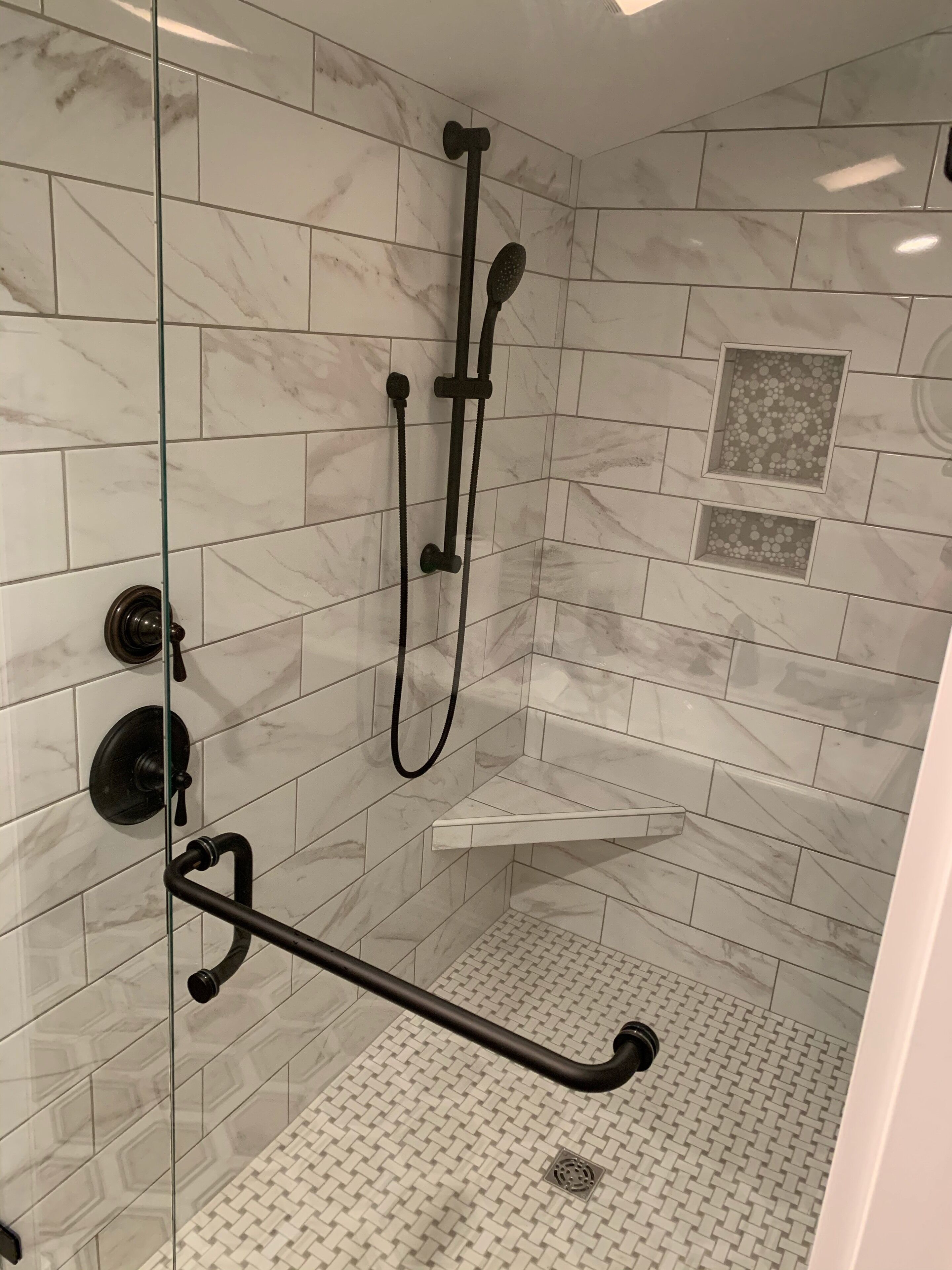 A shower area with a glass door, a handheld showerhead, a wall-mounted faucet, and a small shelf.