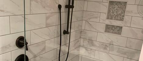 A shower area with a glass door, a handheld showerhead, a wall-mounted faucet, and a small shelf.