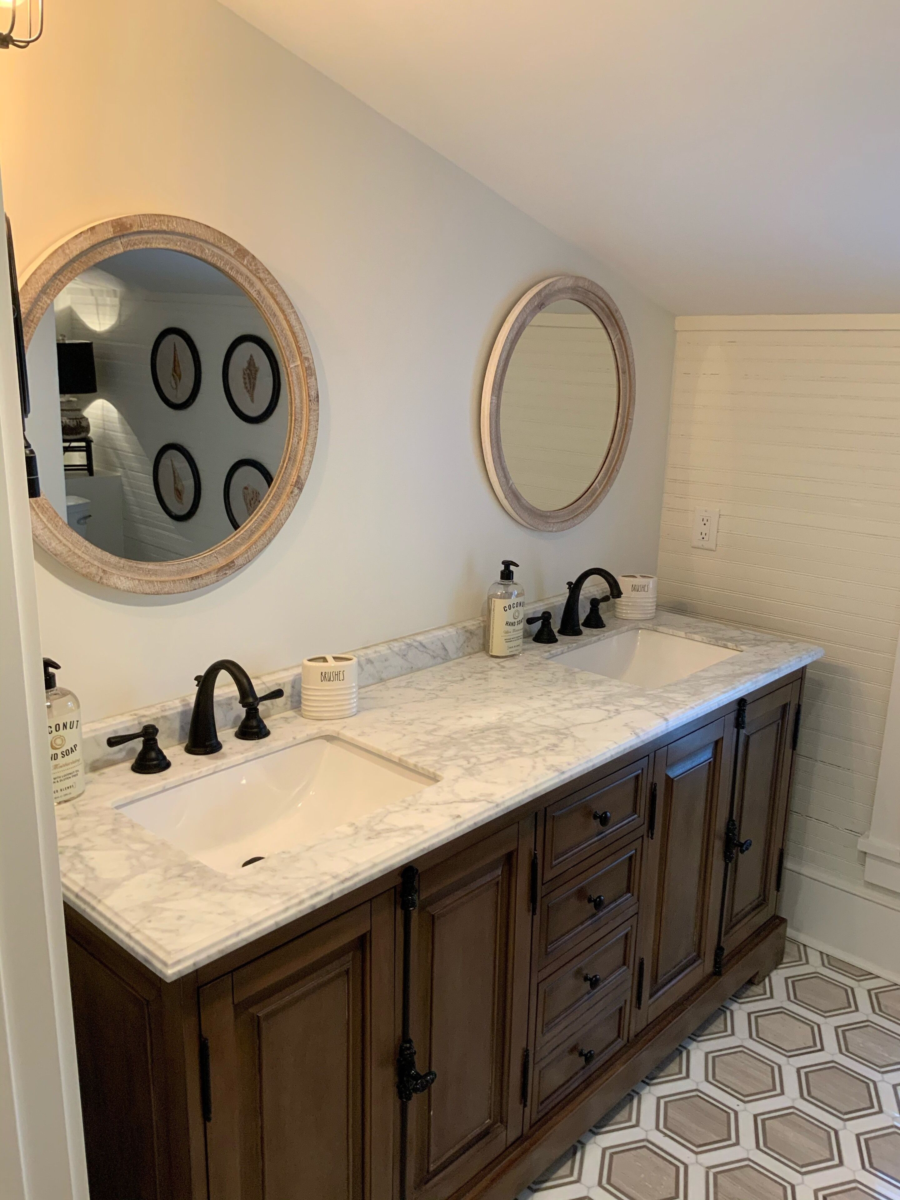 A bathroom with a double sink, two round mirrors, wooden cabinets, and a marble countertop.