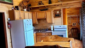 Interior de una cabaña con paredes de madera, un ventilador de techo, un refrigerador, una mesa de comedor y un sofá.