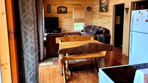 Interior acogedor de una cabaña con techo de madera, televisor, sofá y mesa de comedor.