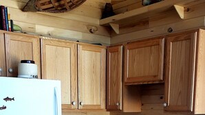 Una cocina de madera con una mesa y sillas de madera, un refrigerador blanco, una cafetera y una estantería con objetos decorativos.