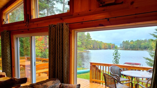 Interior acogedor de una cabaña con un amplio ventanal con vistas a un lago y un área de terraza.