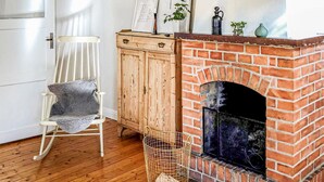 Une pièce avec une cheminée en briques, un meuble en bois, un fauteuil à bascule blanc et un panier en osier.
