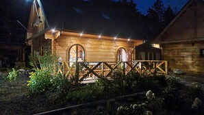 A rustic wooden building with a balcony and arched windows, surrounded by a garden at night. - 4 bedroom stunning home in Ustka (Ustka)